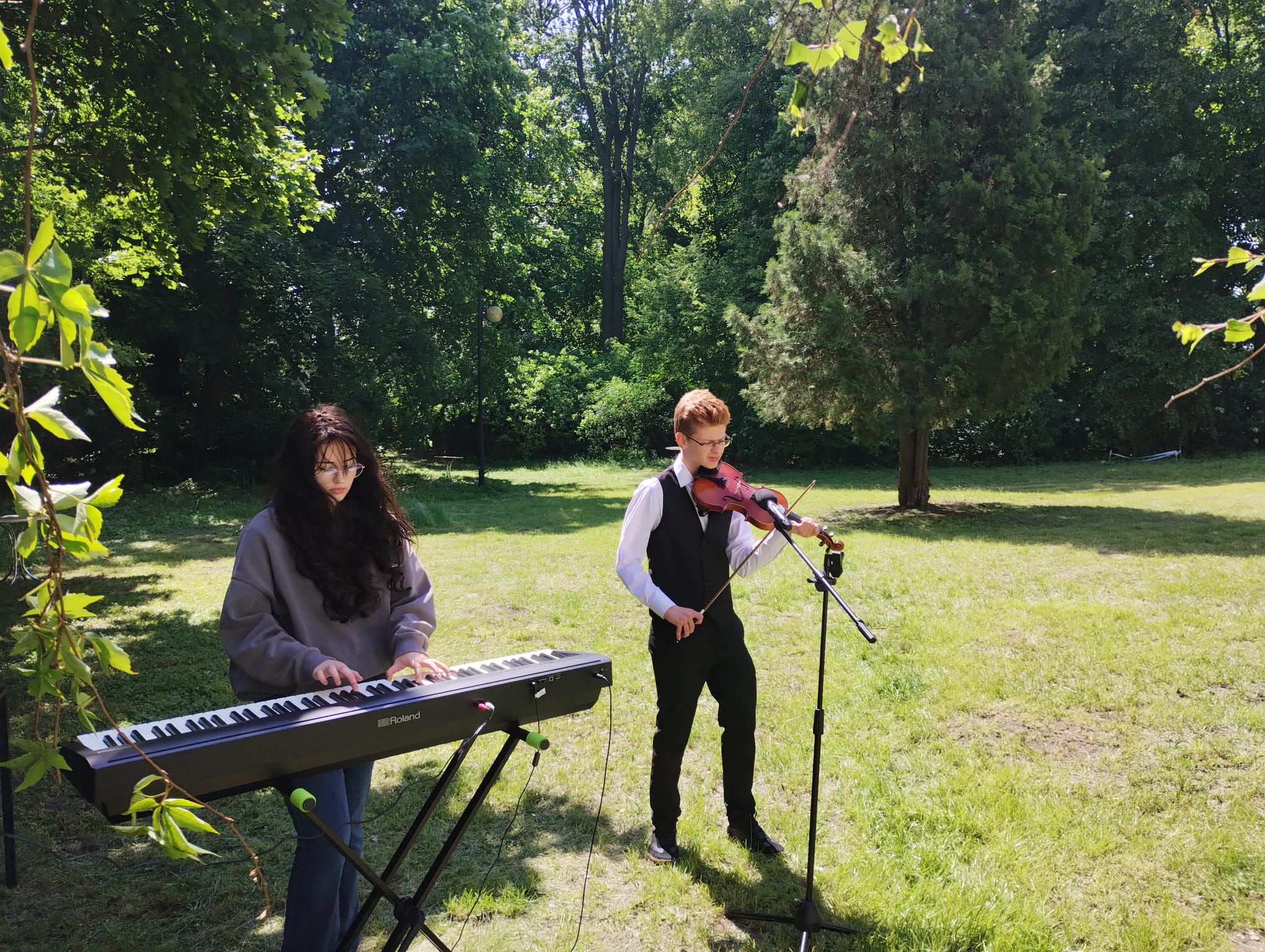 Koncert w plenerze, uczeń gra na skrzypcach z towarzyszeniem dziewczyny grającej na pianinie 