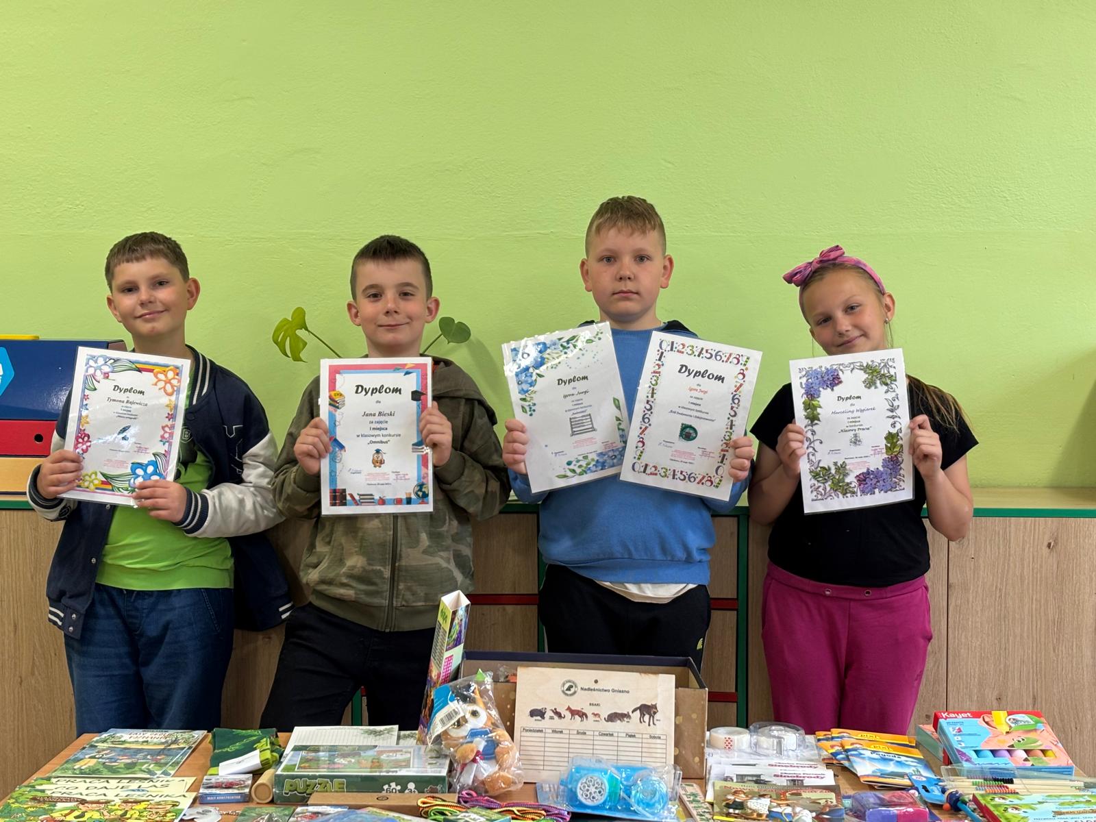 Zdjęcie grupy laureatów trzymających dyplomy przy stole z nagrodami