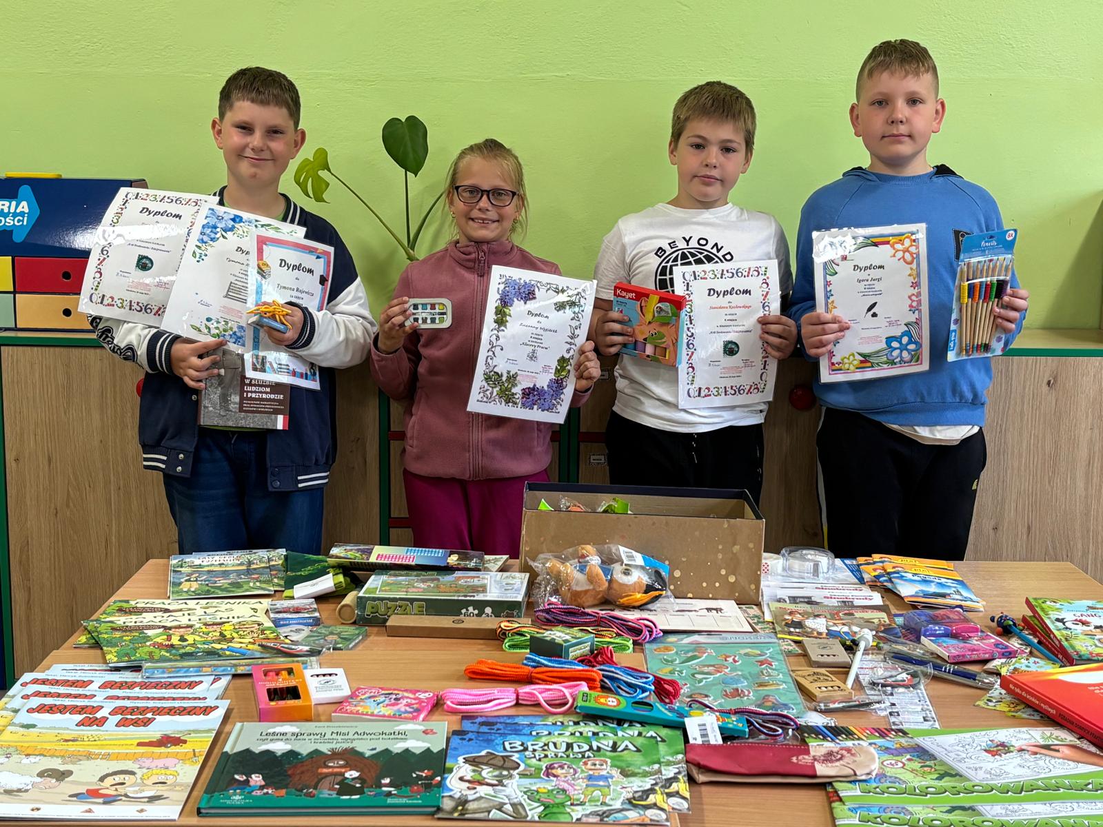 Zdjęcie grupy laureatów trzymających dyplomy przy stole z nagrodami