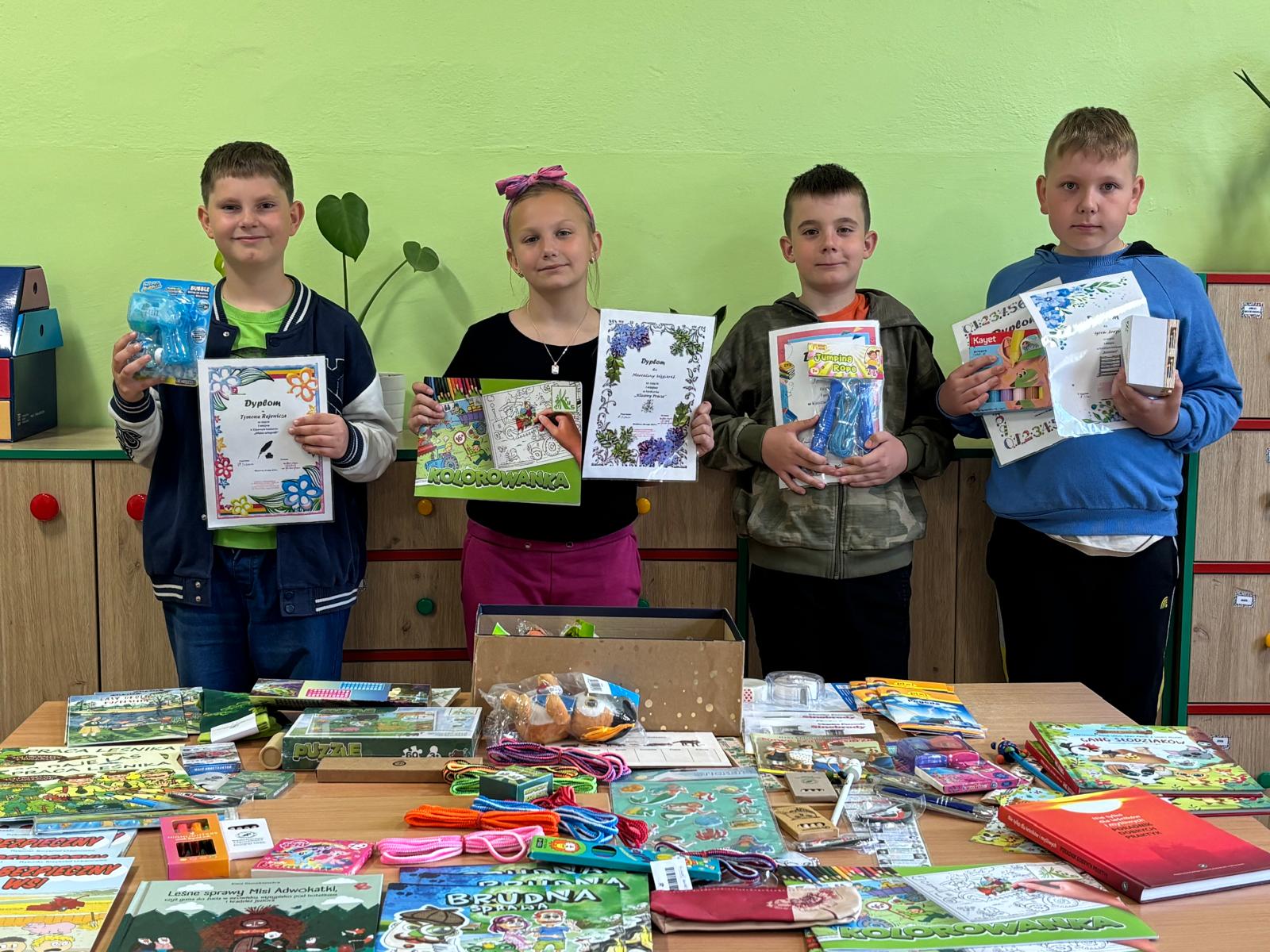 Zdjęcie grupy laureatów trzymających dyplomy przy stole z nagrodami