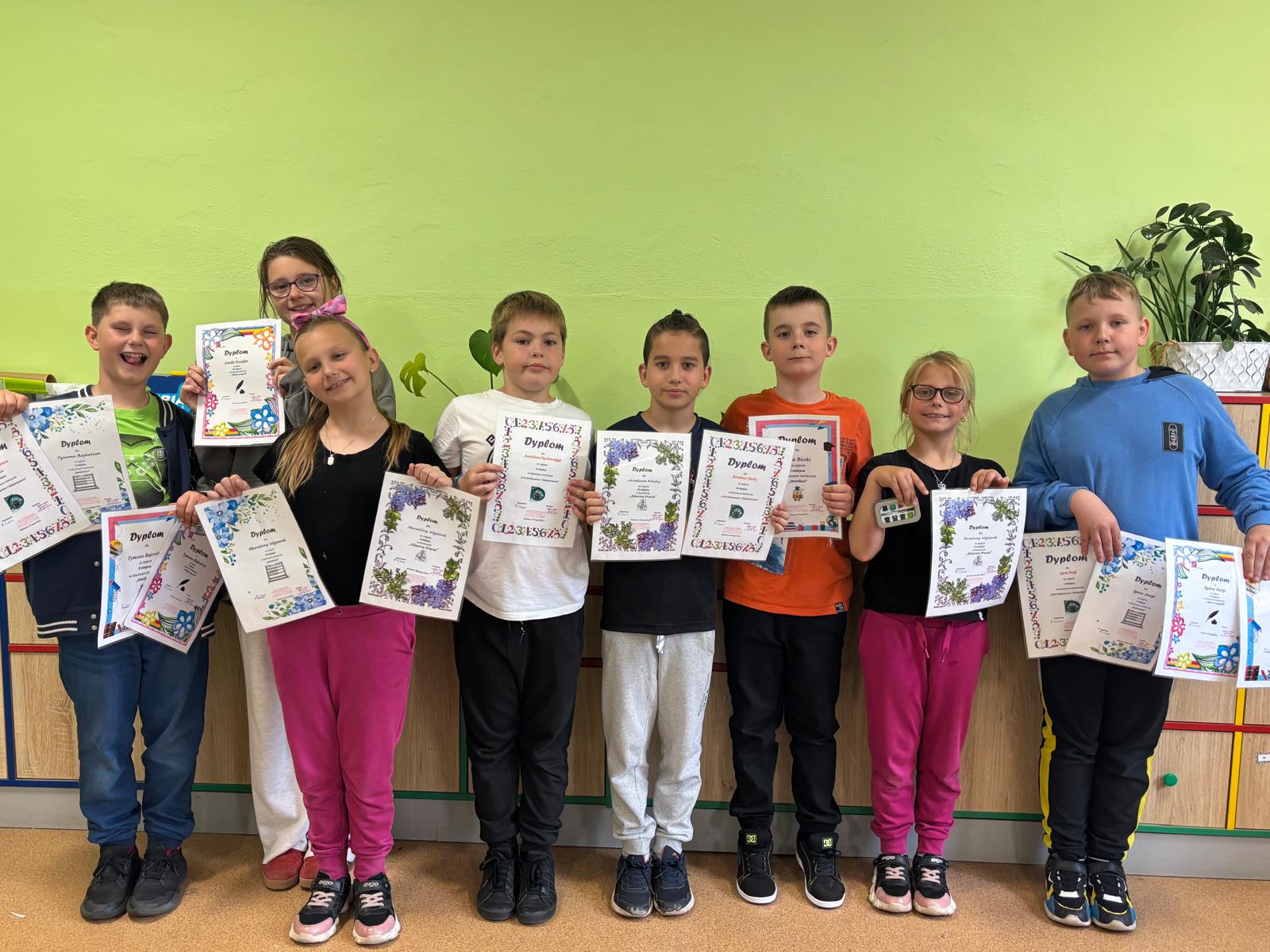 Zdjęcie grupy laureatów trzymających dyplomy przy stole z nagrodami