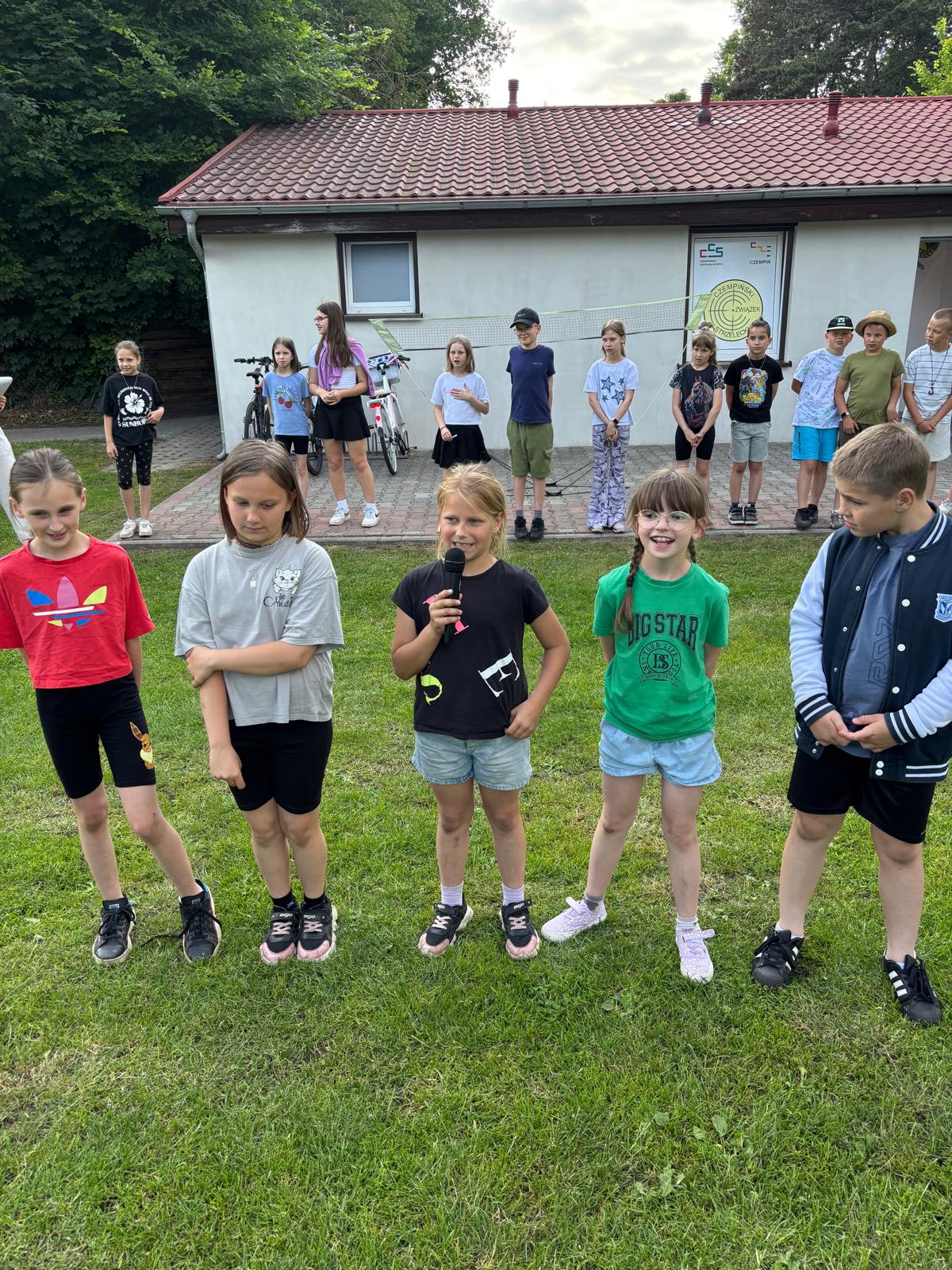 Grupa pięciu uczniów, dziewczyna w środku grupy trzyma mikrofon