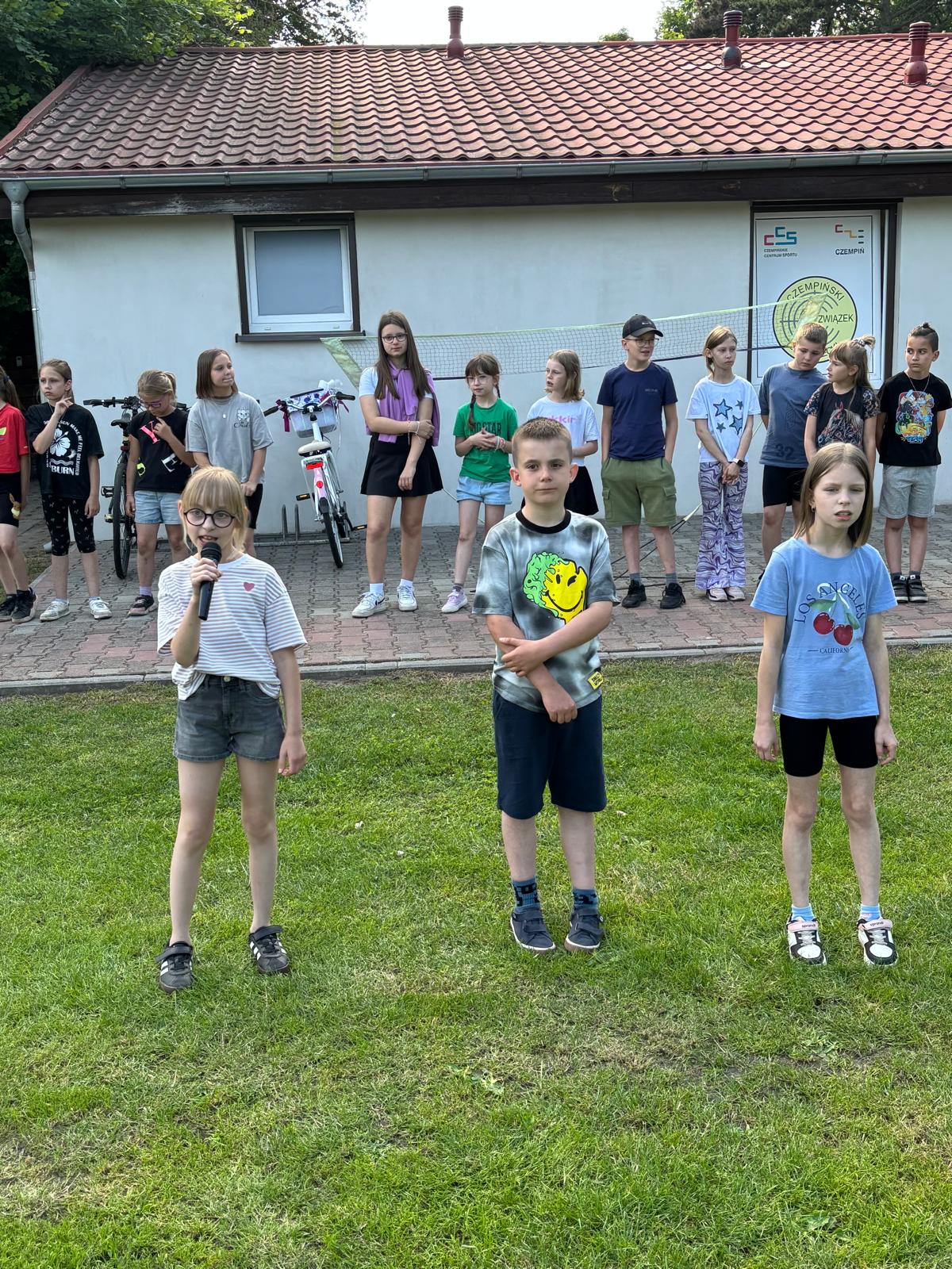 Grupa trzech uczniów, dziewczyna po lewej mówi do mikrofonu